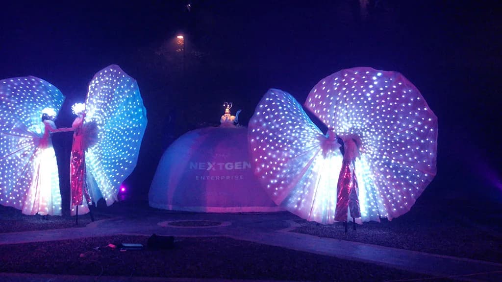 Des artistes en costumes lumineux aux ailes en éventail devant le dôme NextGen Enterprise, de nuit