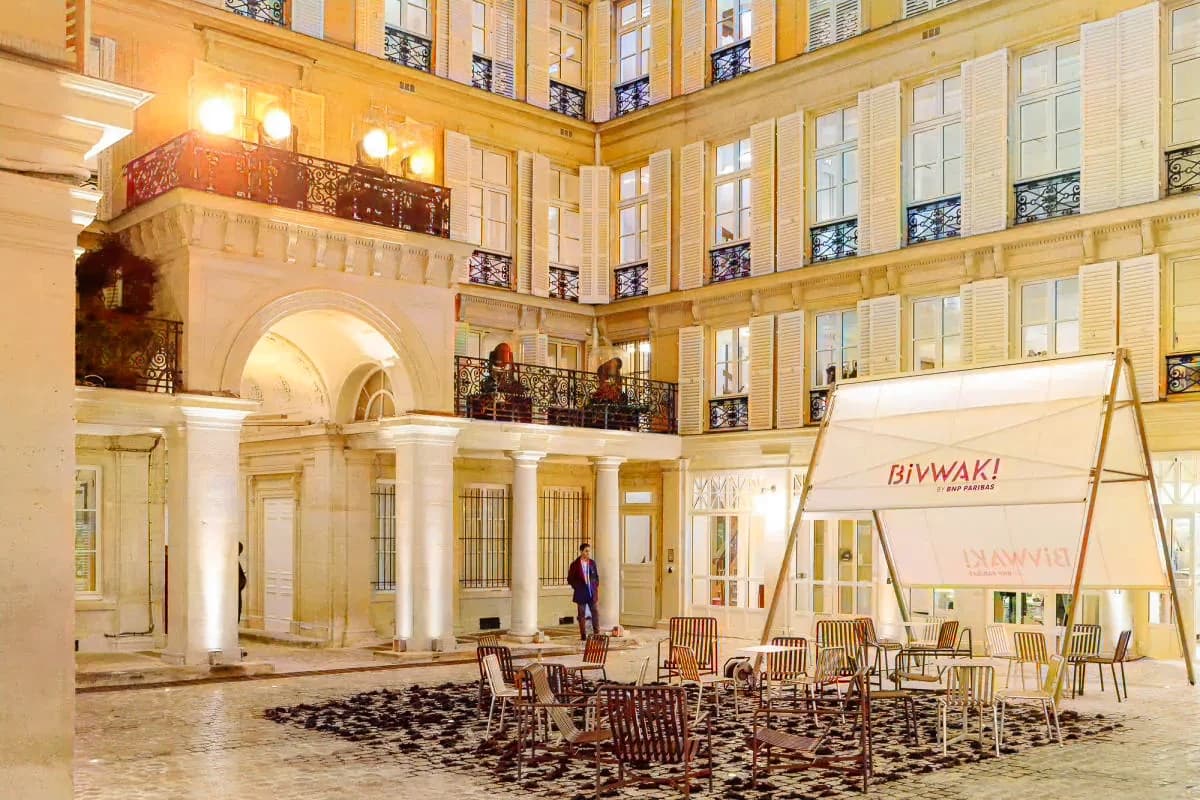 La cour pavée de Bivwak! la nuit, des chaises installées devant un auvent Bivwak!